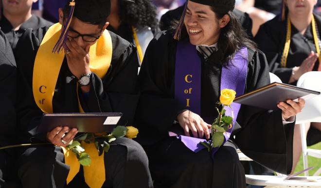 Graduates at the 2018 Commencement Ceremony look at their diplomas in the crowd.