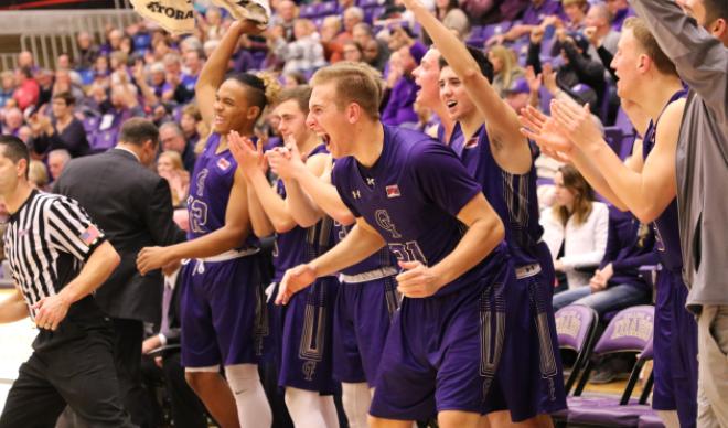 The C of I men's basketball team celebrates on the sidelines.