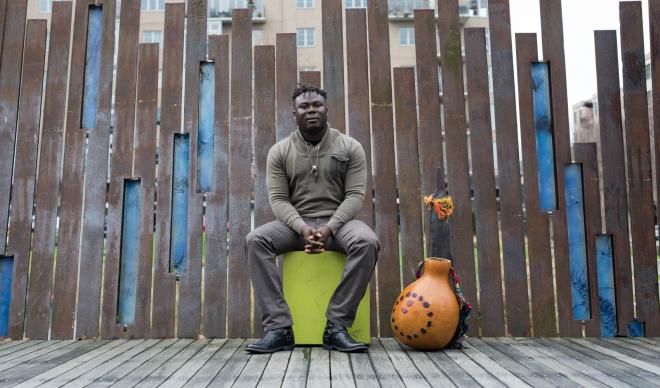 Okaidja Afroso sits on a street alongside a traditional drum.
